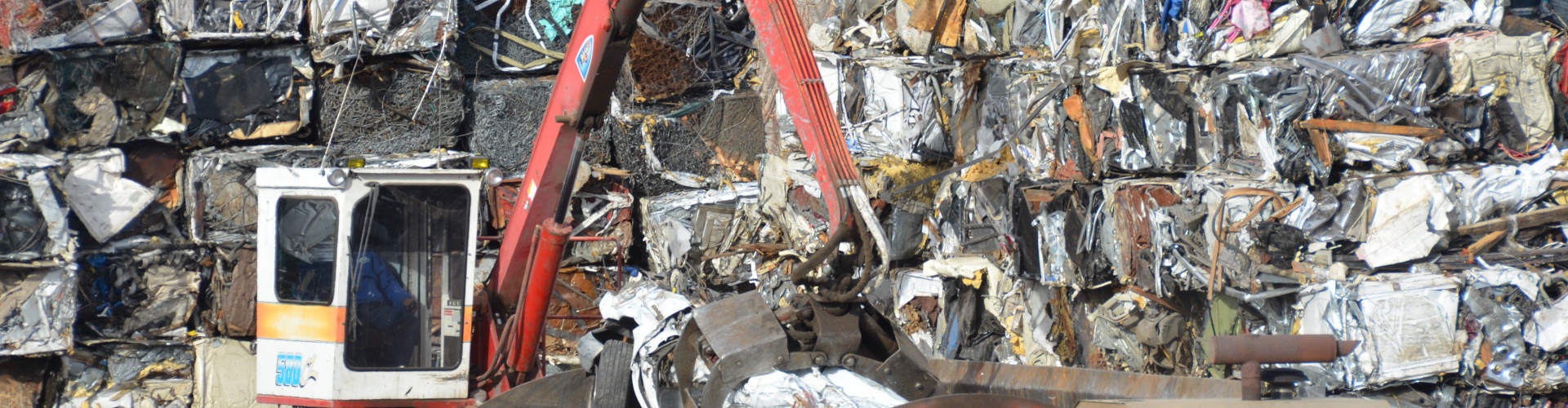 Photo of mechanical claw stacking compressed scrap metal cubes.